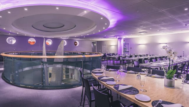 Modern event space with round tables and purple lighting for corporate meetings and gatherings.