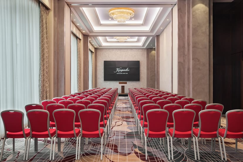 Ballroom 1 at Grand Hotel Kempinski Riga, featuring red chairs for conferences and workshops.