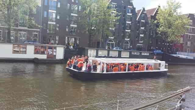 Lively networking event on a boat in Amsterdam's scenic canals with festive orange attire.