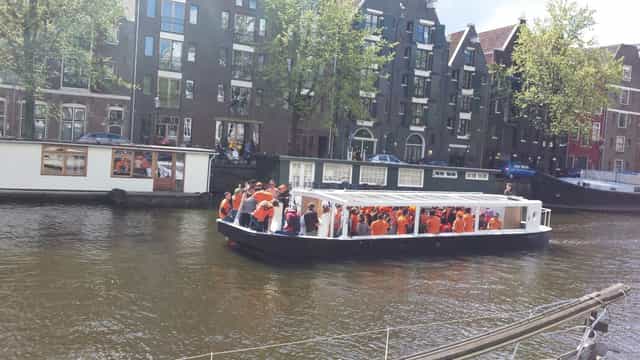 Lively networking event on a boat in Amsterdam's scenic canals with festive orange attire.