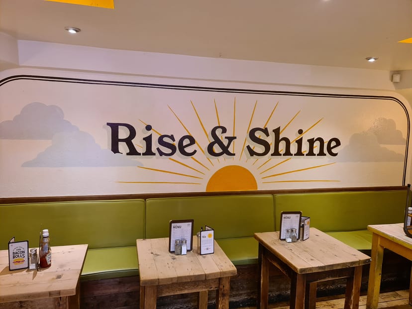 Vibrant café with "Rise & Shine" mural, ideal for morning meetings and casual gatherings.