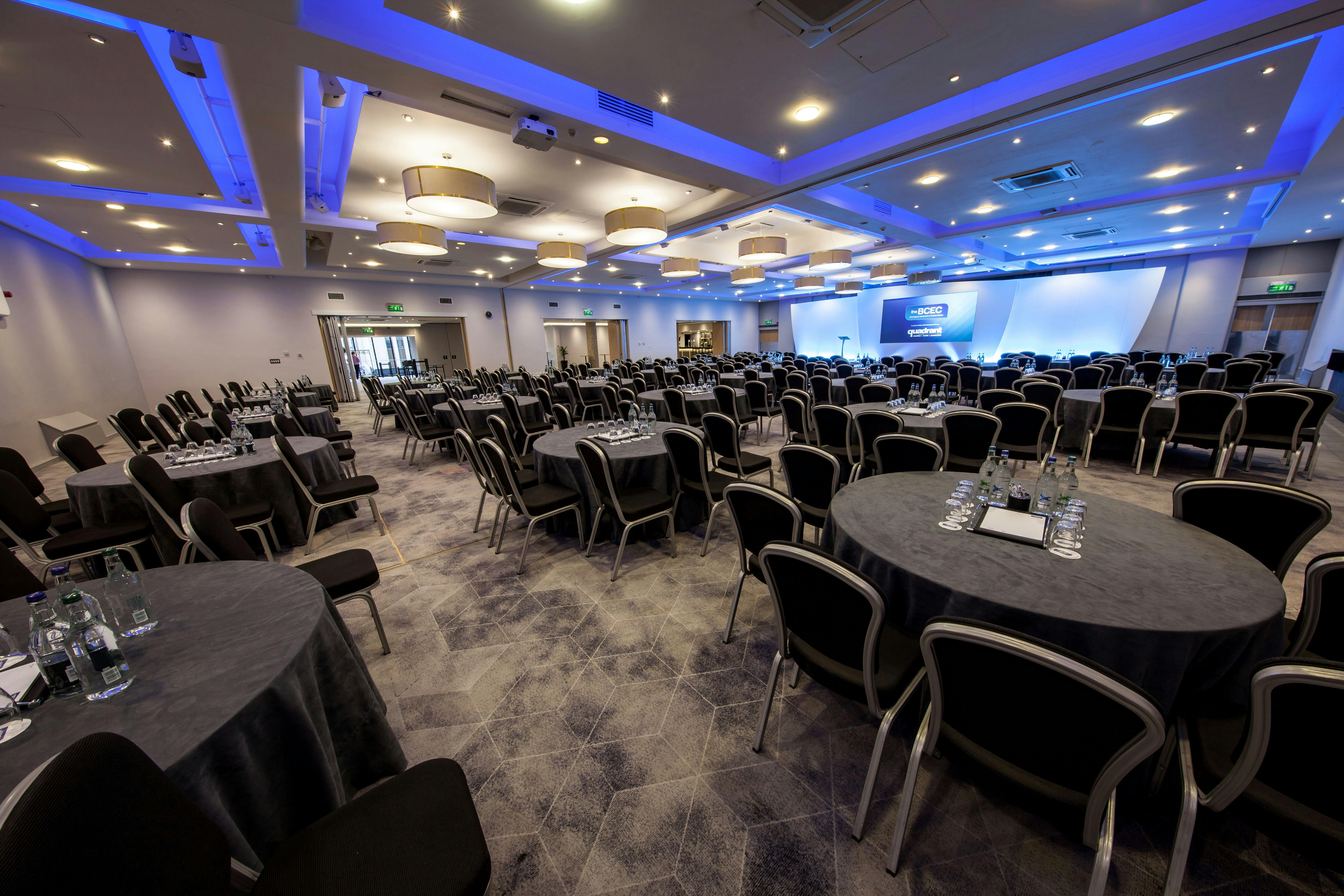 Spacious conference venue at The Mercian, featuring round tables for corporate events.