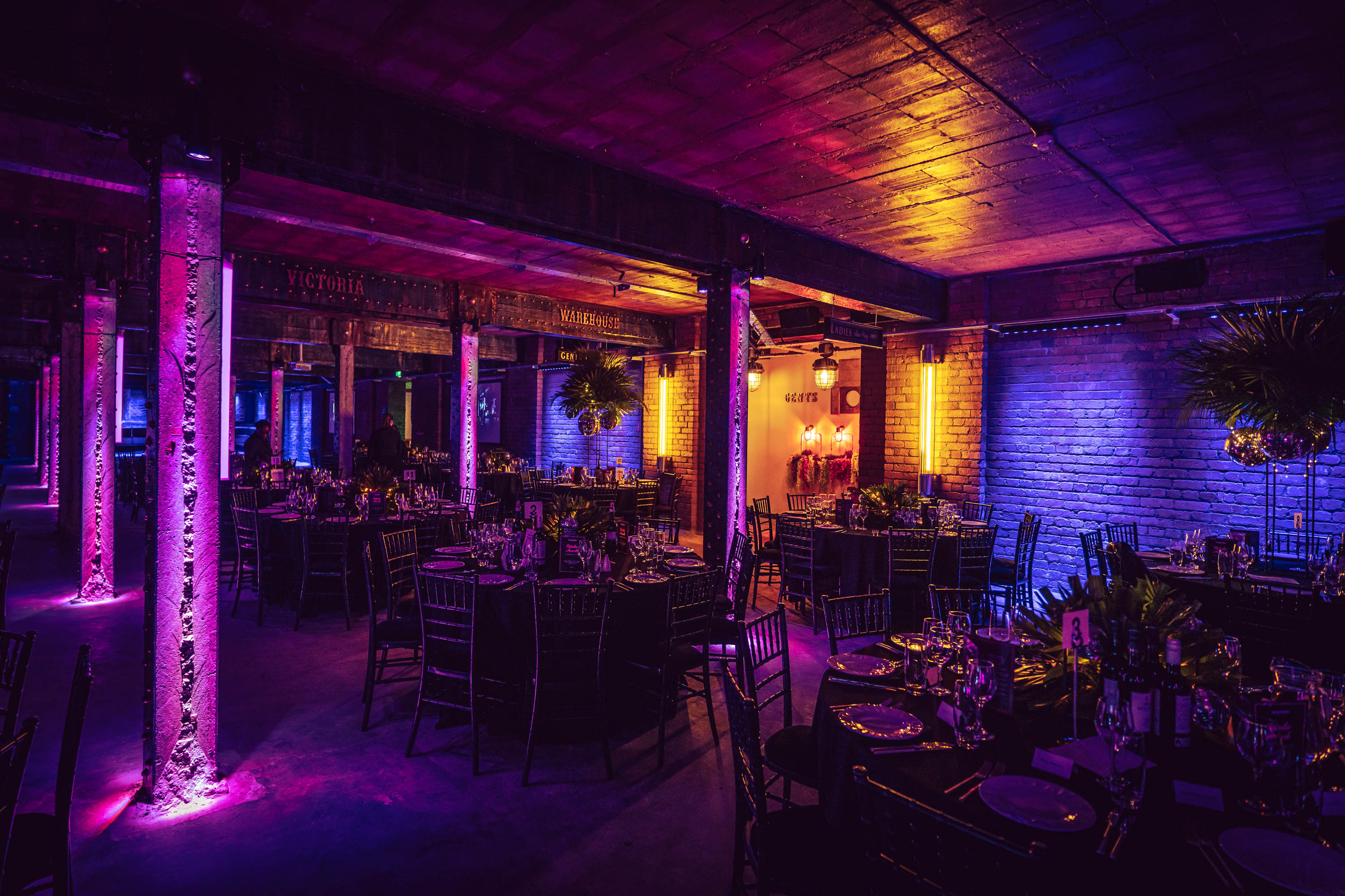 Elegant event space at Tobacco Stores, featuring vibrant uplighting and stylish table settings.