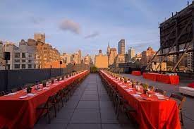 Rooftop event space at Hudson Mercantile with red linens and NYC skyline, ideal for gatherings.