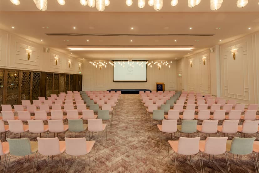 Ballroom at Osprey Hotel set for a conference with pastel chairs and elegant lighting.
