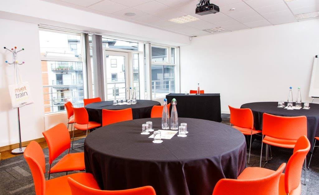 Modern meeting space with round tables and orange chairs for workshops and presentations.