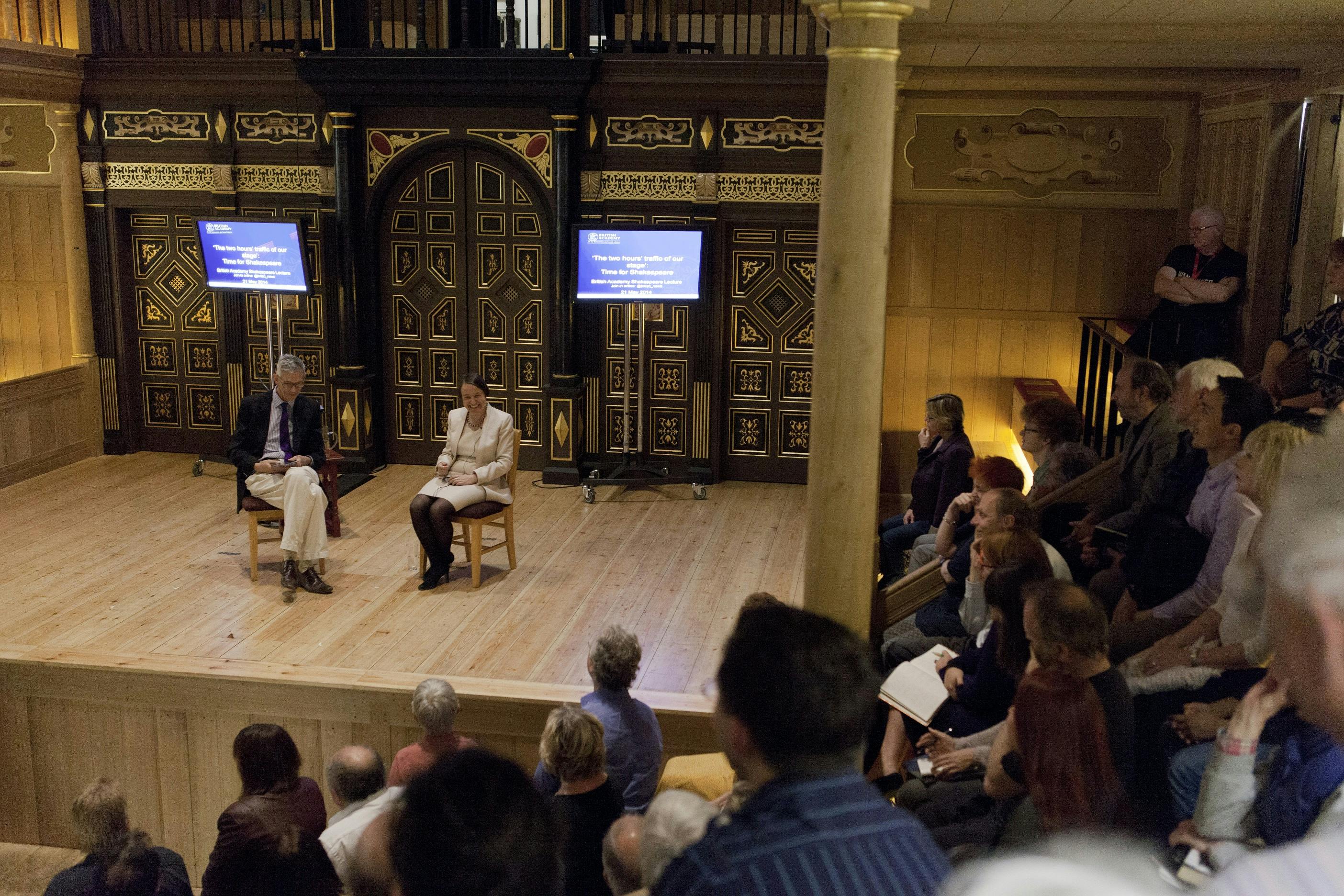 "Panel discussion at Sam Wanamaker Theatre with engaging speakers and warm wooden decor."