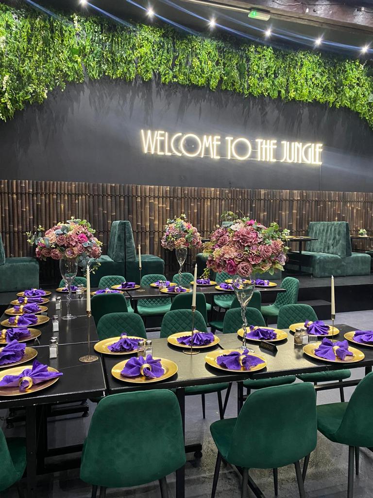 Elegant event space at Jungle Bar & Grill with purple napkins and neon sign. - Banner