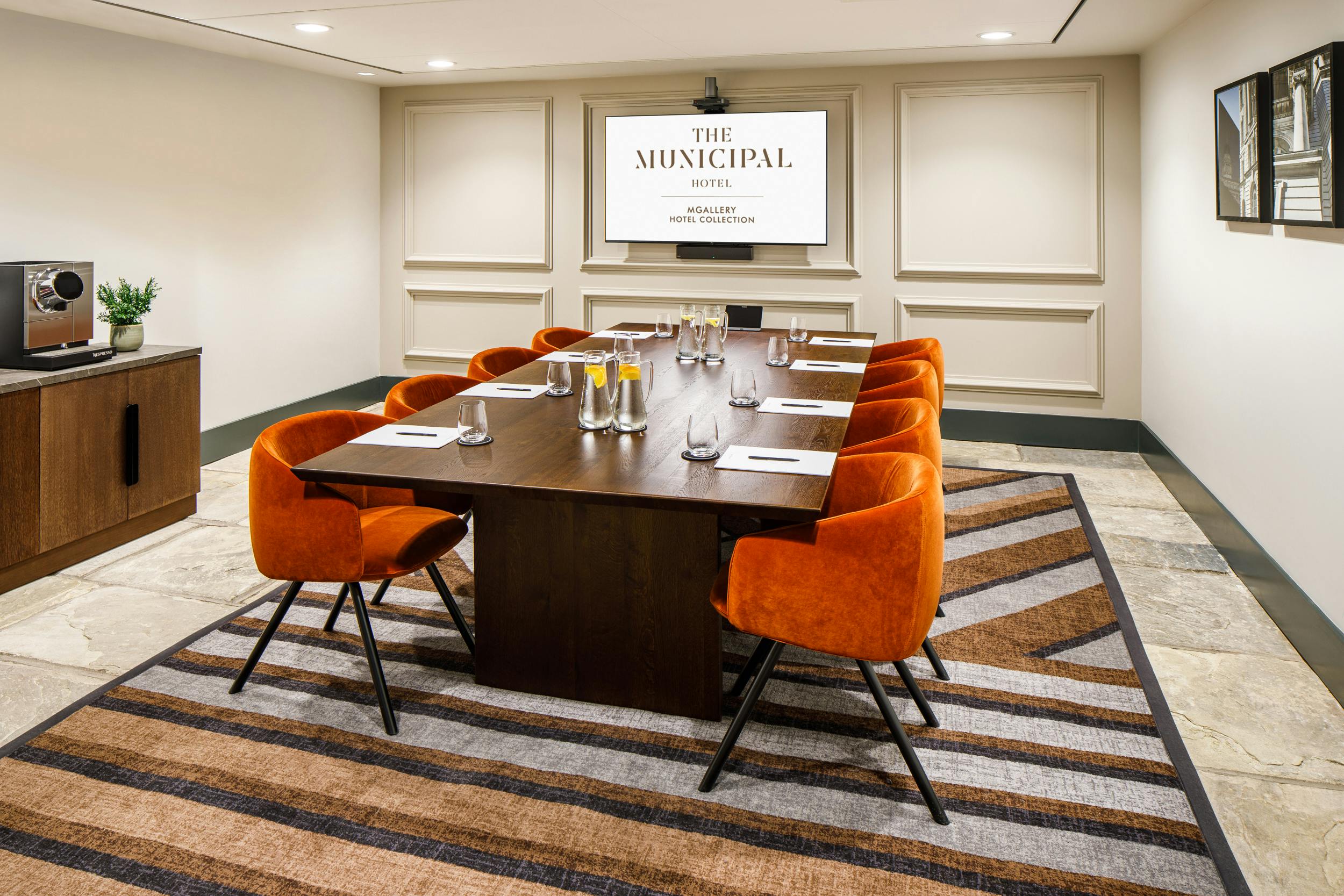 Modern meeting room at Municipal Hotel Liverpool with wooden table and orange chairs.