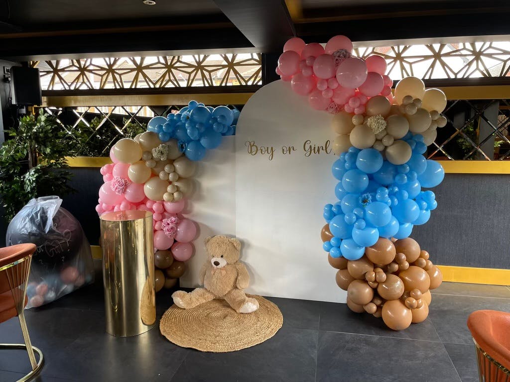 Gender reveal event backdrop with pastel balloon arch and teddy bear decor.