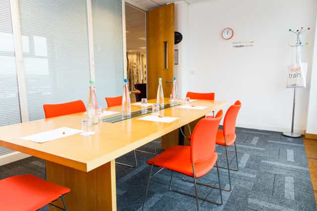 Modern meeting room in Leeds with wooden table and vibrant orange chairs for collaboration.