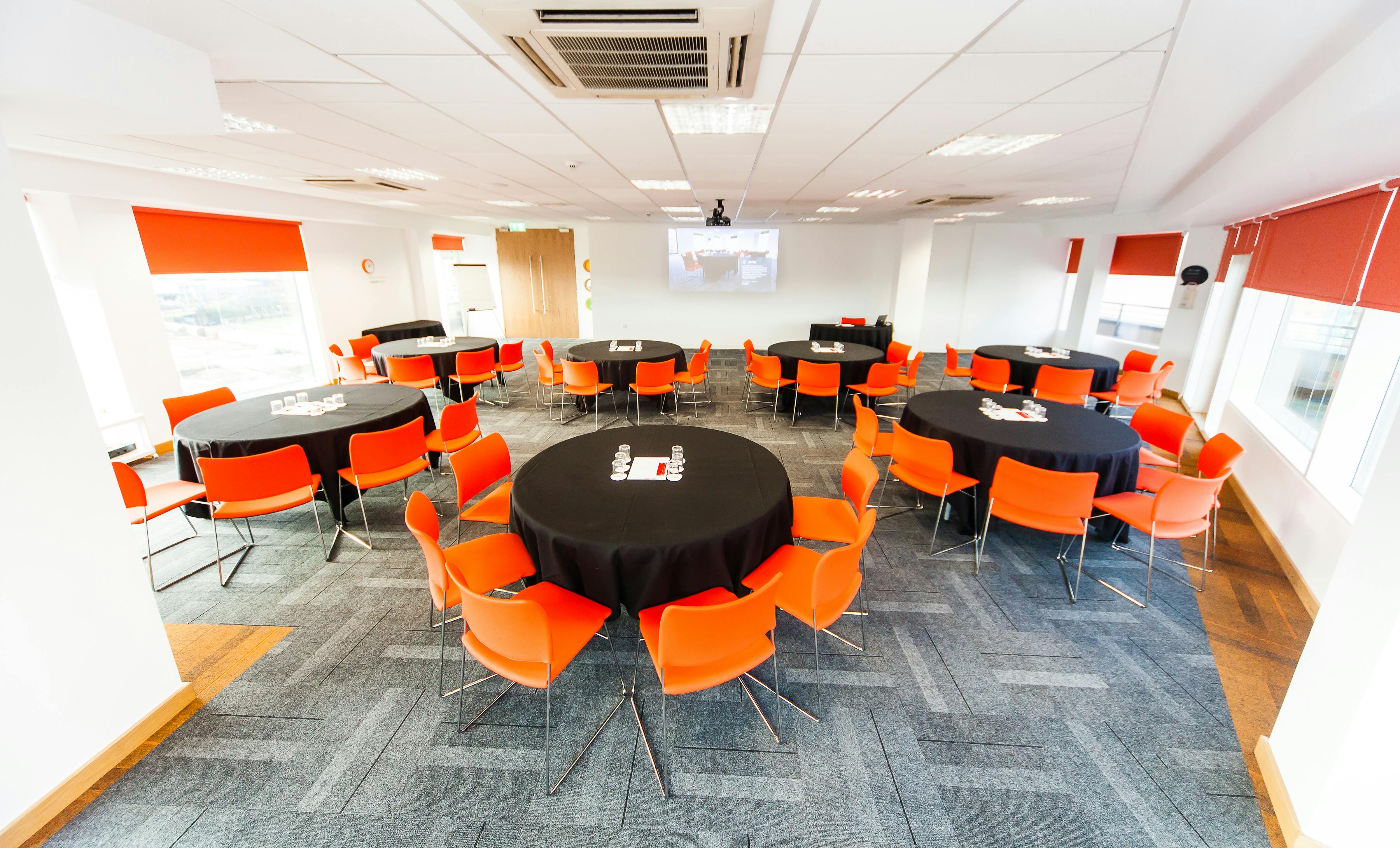 Versatile meeting space in Leeds with round tables and vibrant orange chairs for workshops.