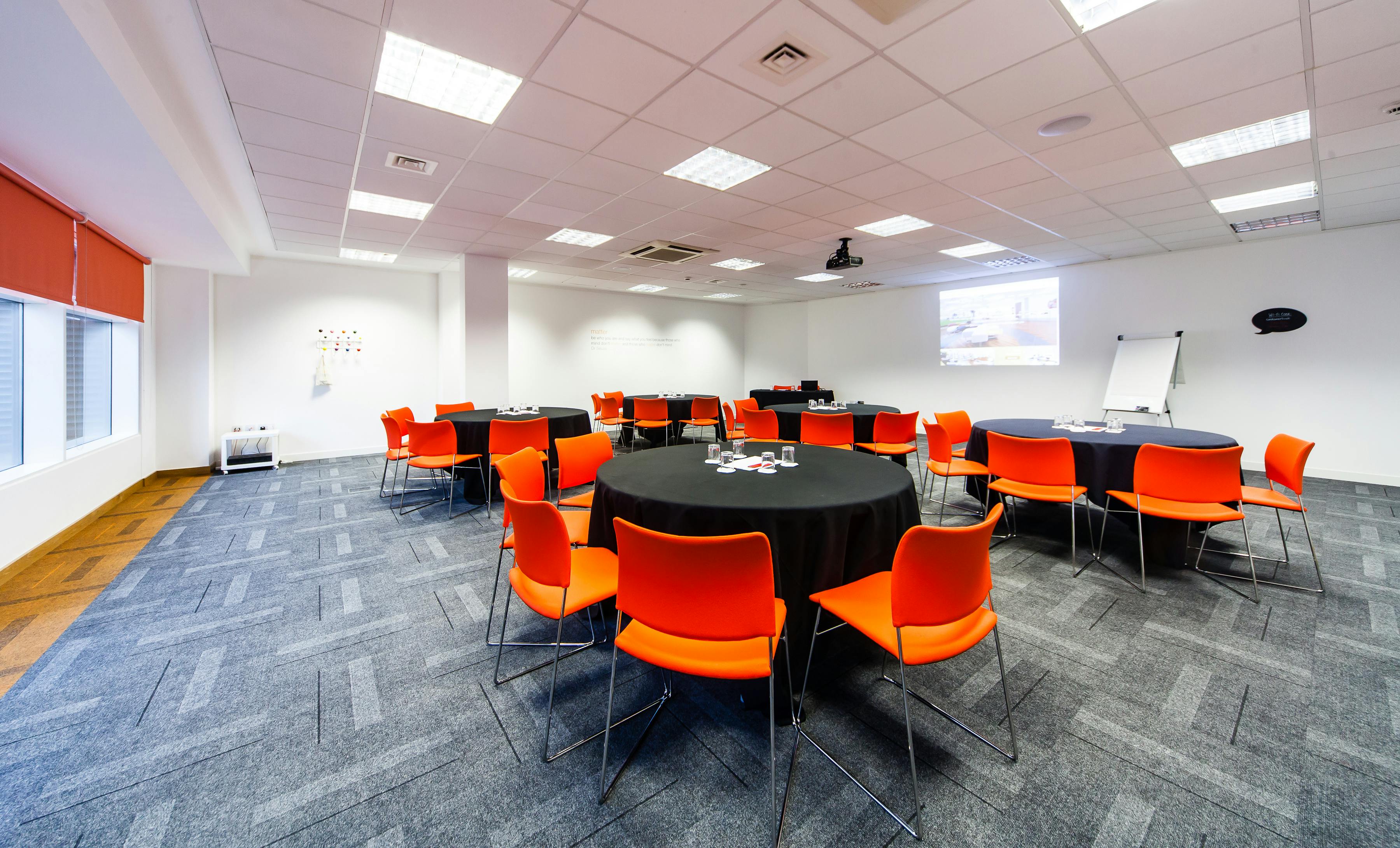 Modern meeting space with round tables, orange chairs for workshops and conferences.