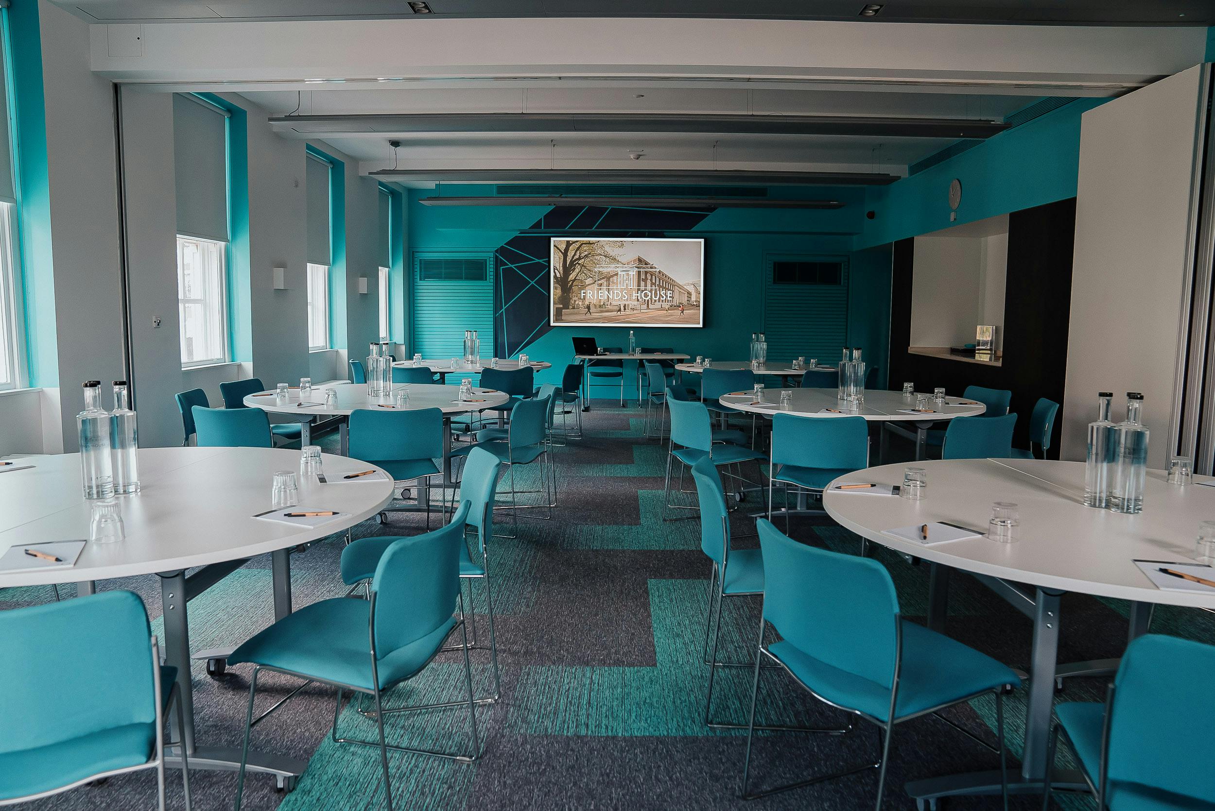 Modern meeting room with circular tables and turquoise accents for workshops and collaboration.