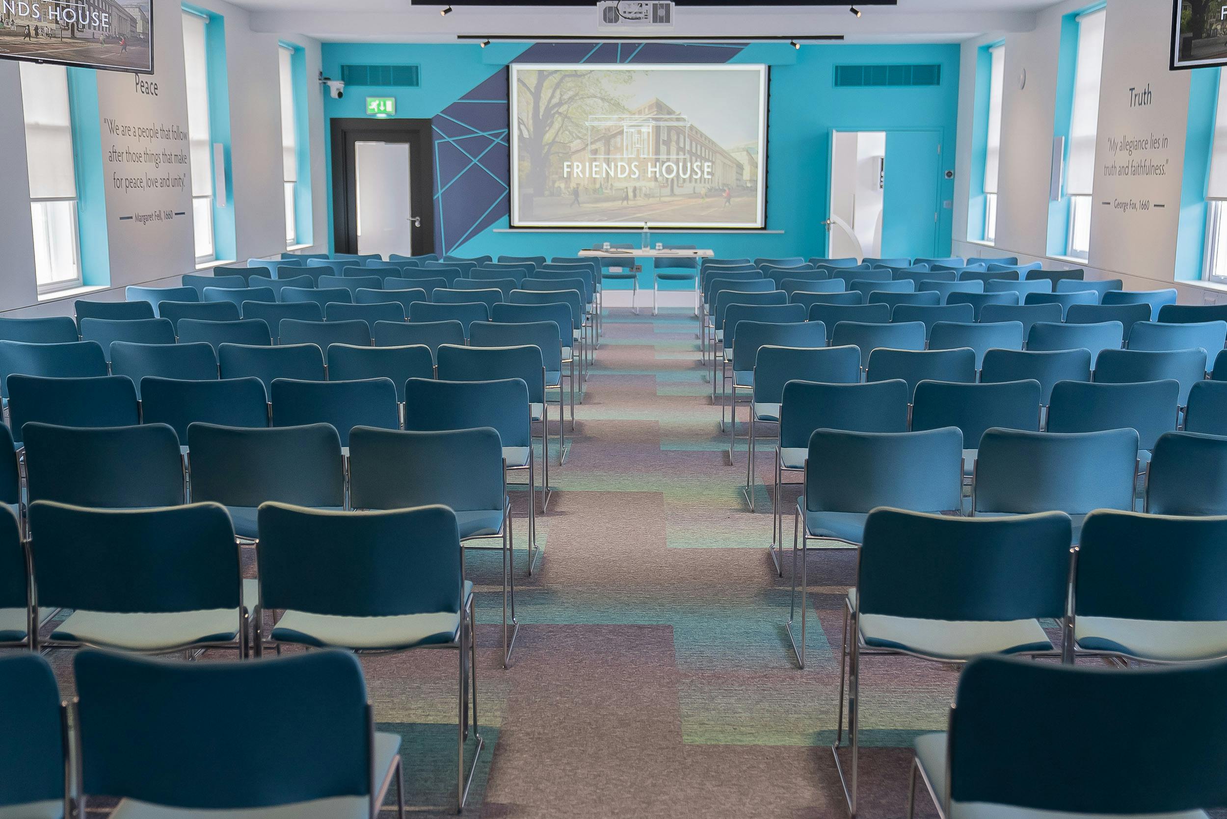 Event space with blue chairs and large screen, ideal for conferences and workshops.