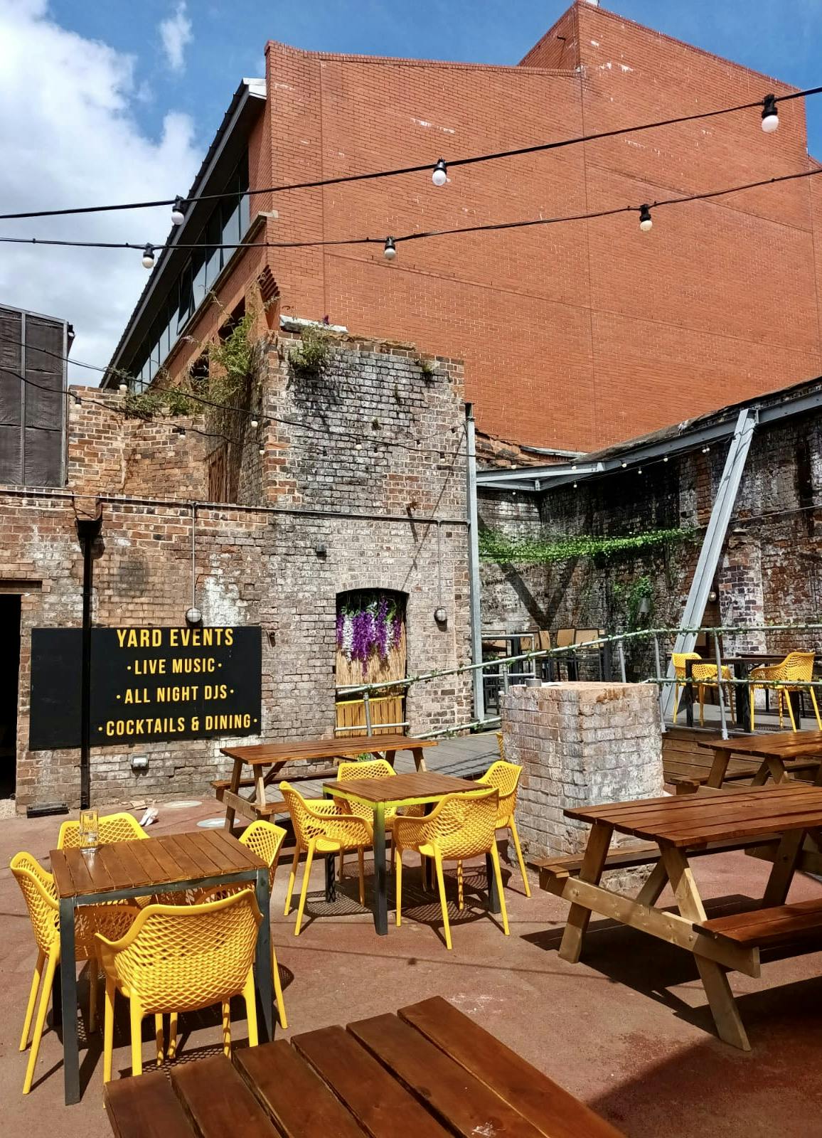 Vibrant outdoor event space at The Yard, featuring rustic brick and yellow seating.