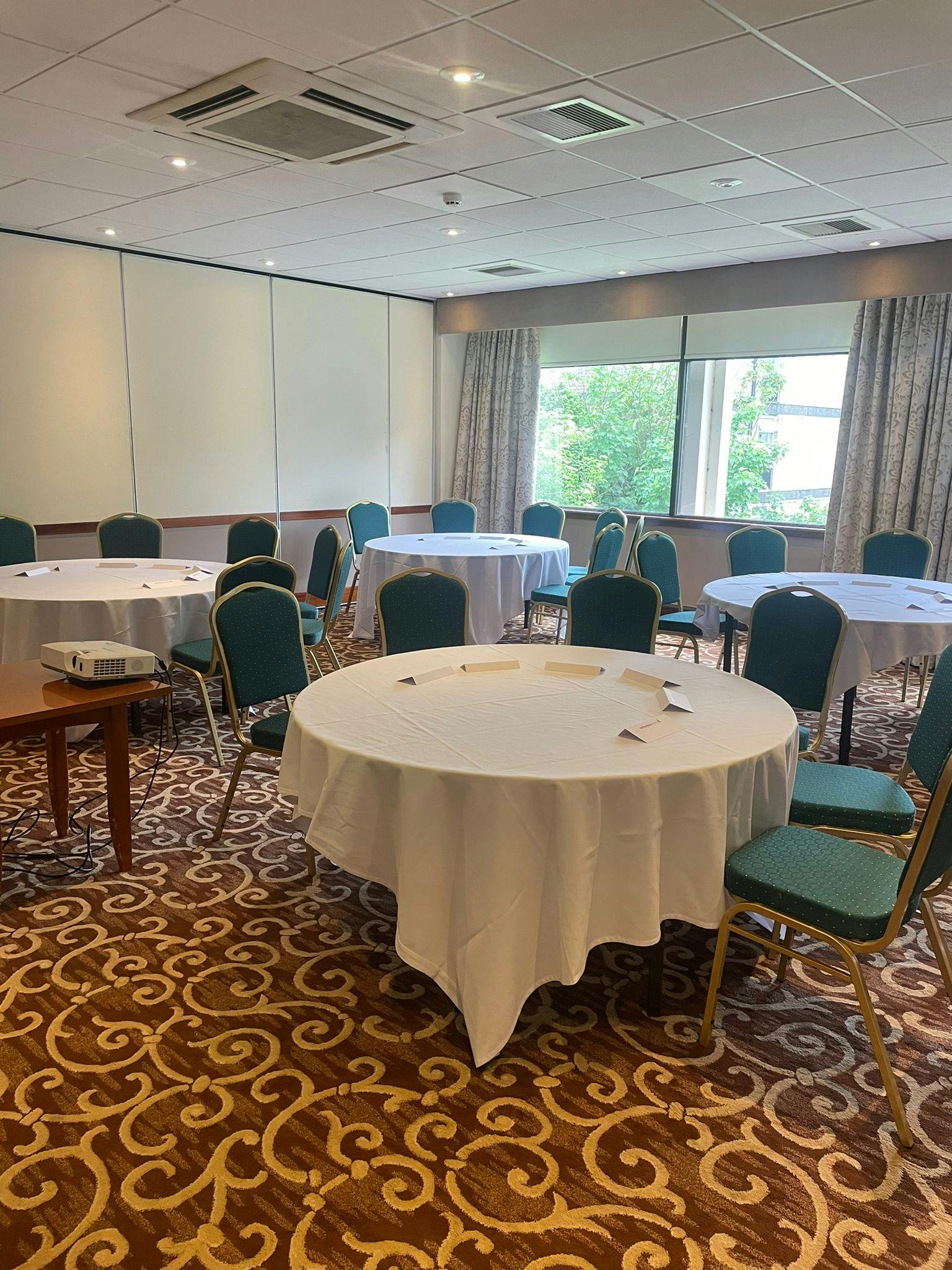 Bright meeting room with round tables at Leeds Bradford Airport Hotel for workshops.