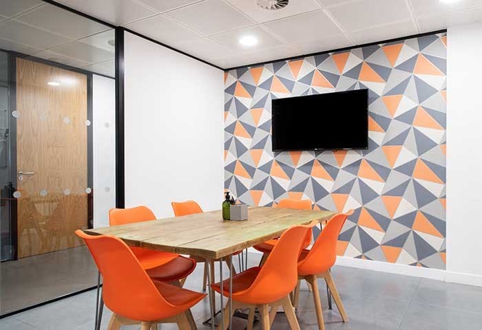 Modern meeting room with geometric wall, orange chairs for collaborative workshops.