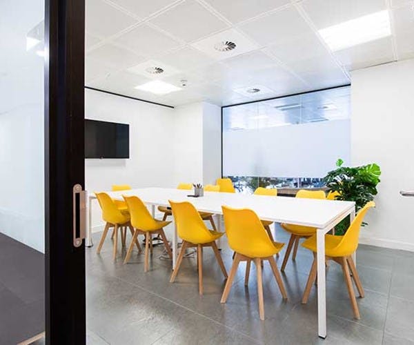 Modern meeting room with large white table and yellow chairs, ideal for presentations.