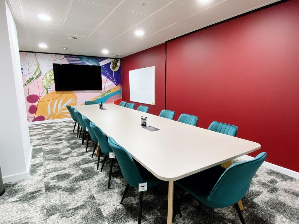 Modern meeting room with teal chairs, red wall, ideal for workshops and presentations.