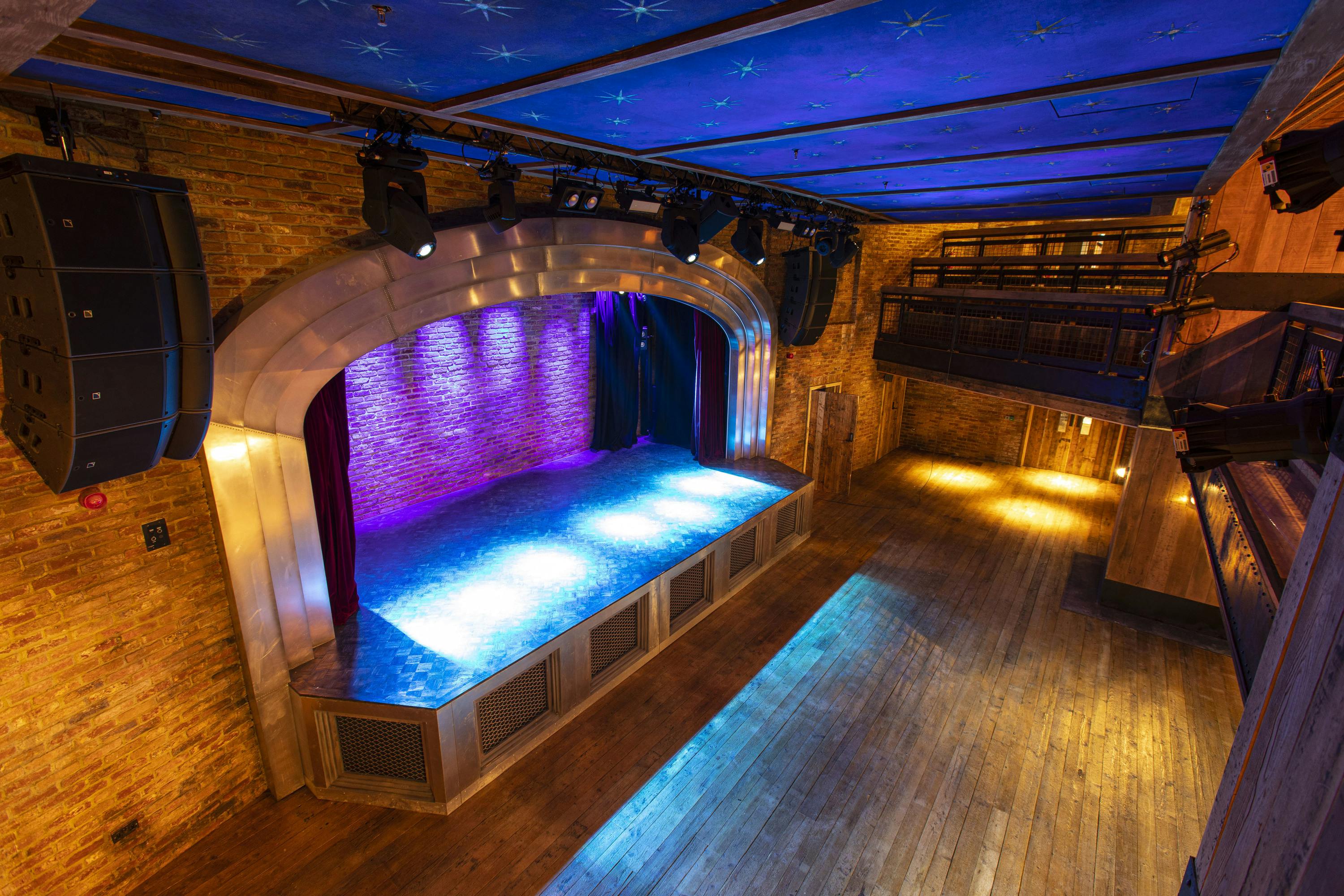 Versatile event space with vibrant stage lighting and exposed brick walls for performances.