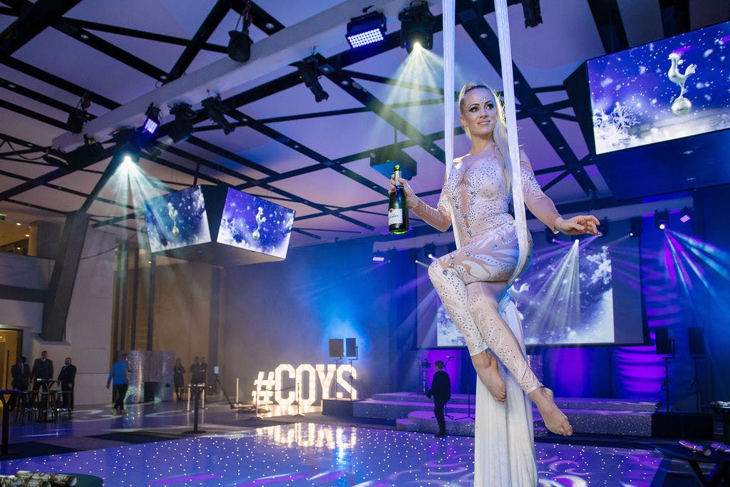 Aerial performer at Christmas party in Tottenham Hotspur Stadium, vibrant event space.