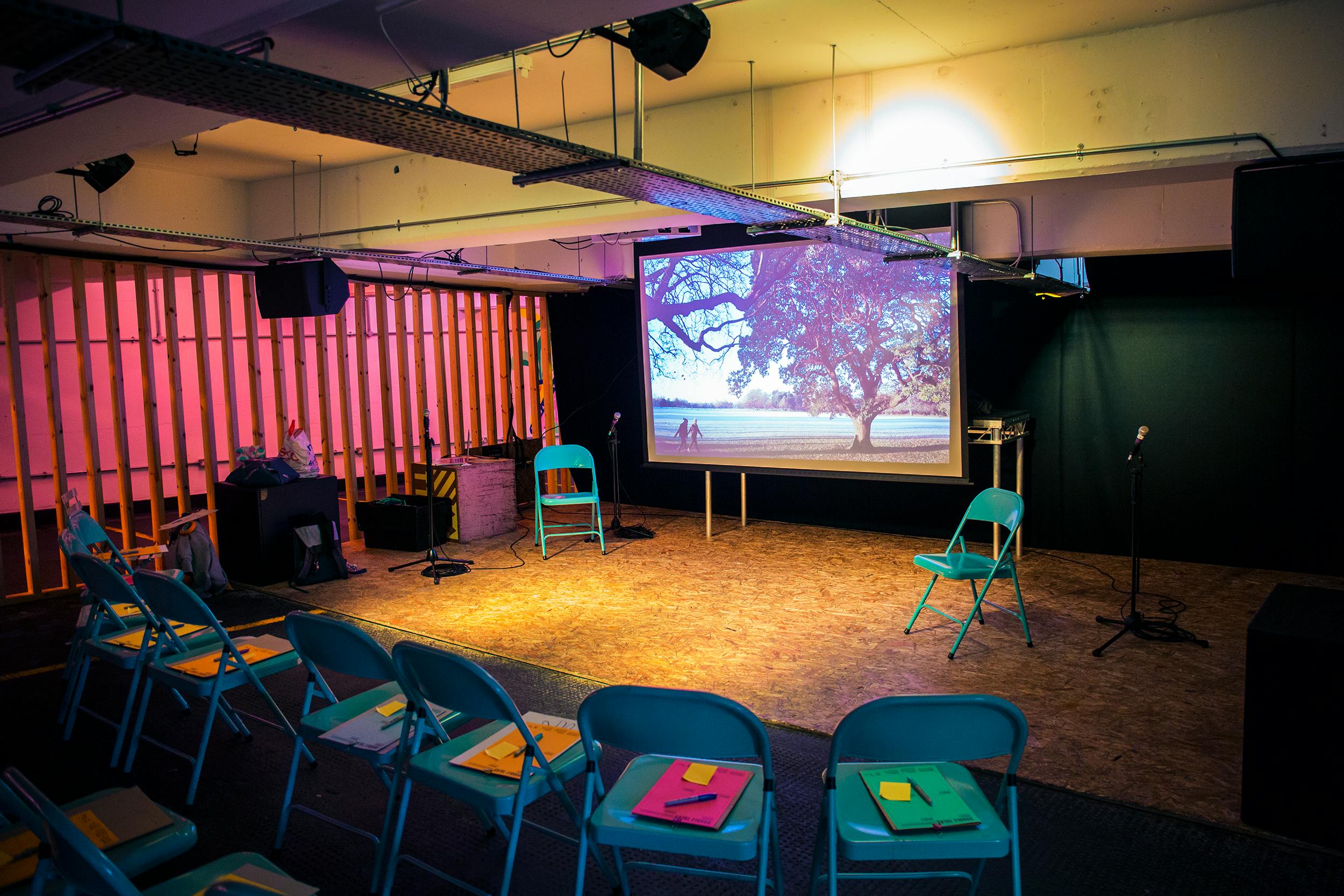 Intimate event space in Peckham Levels with teal chairs and large screen for presentations.