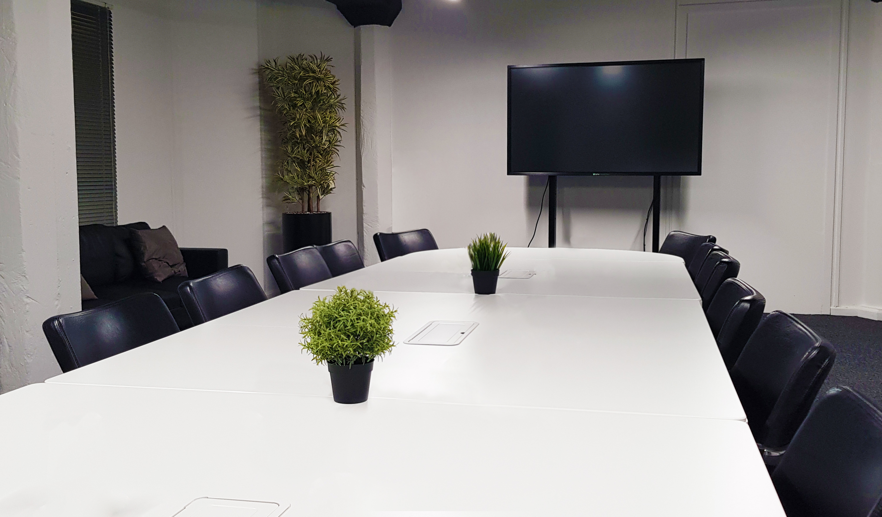 Modern Glasgow training room with white table, black chairs, ideal for meetings and presentations.