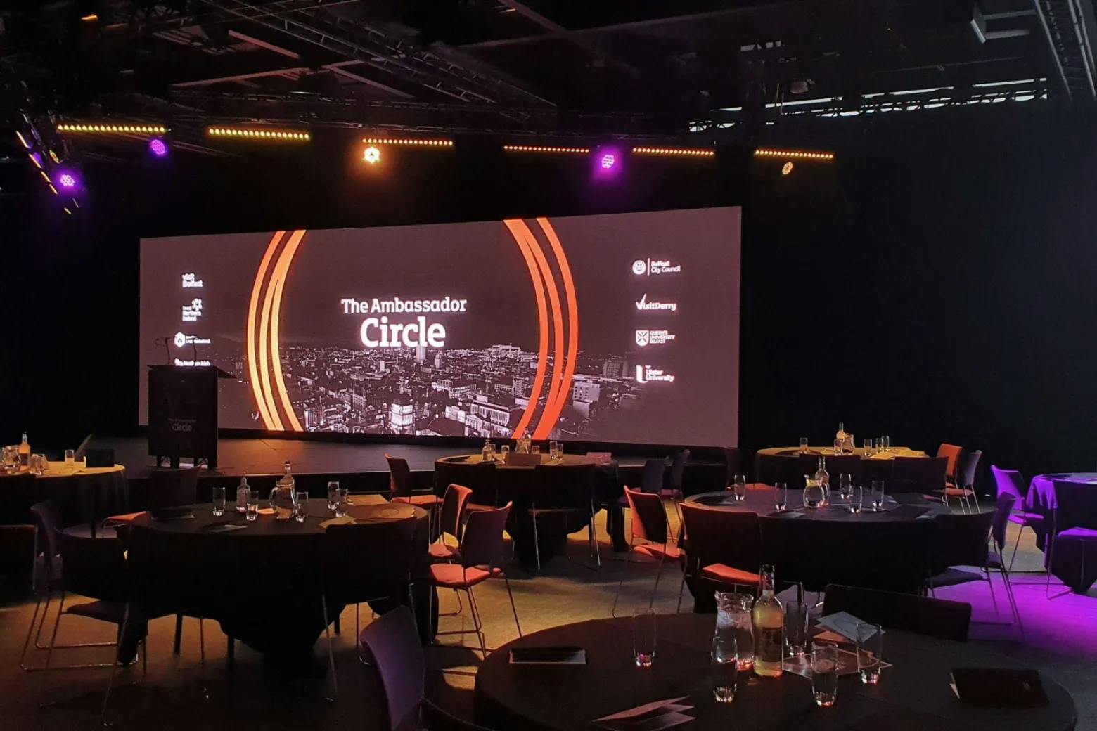 Event space at ICC Belfast with round tables and a large screen for networking events.