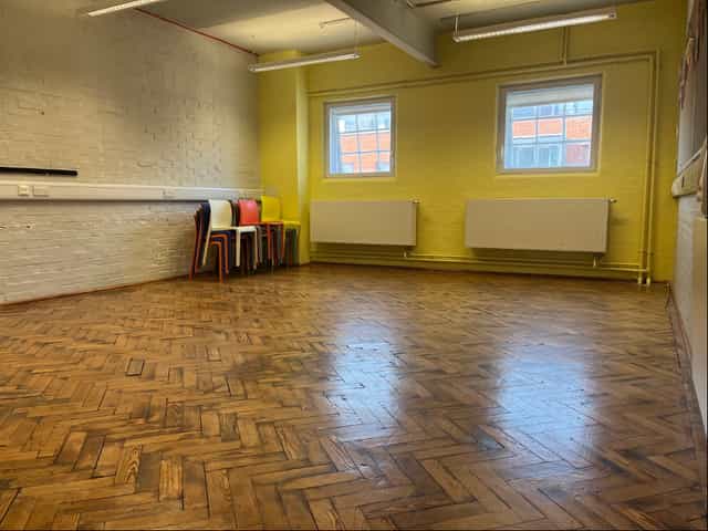 Versatile rehearsal room with wooden floor and bright yellow walls for workshops.