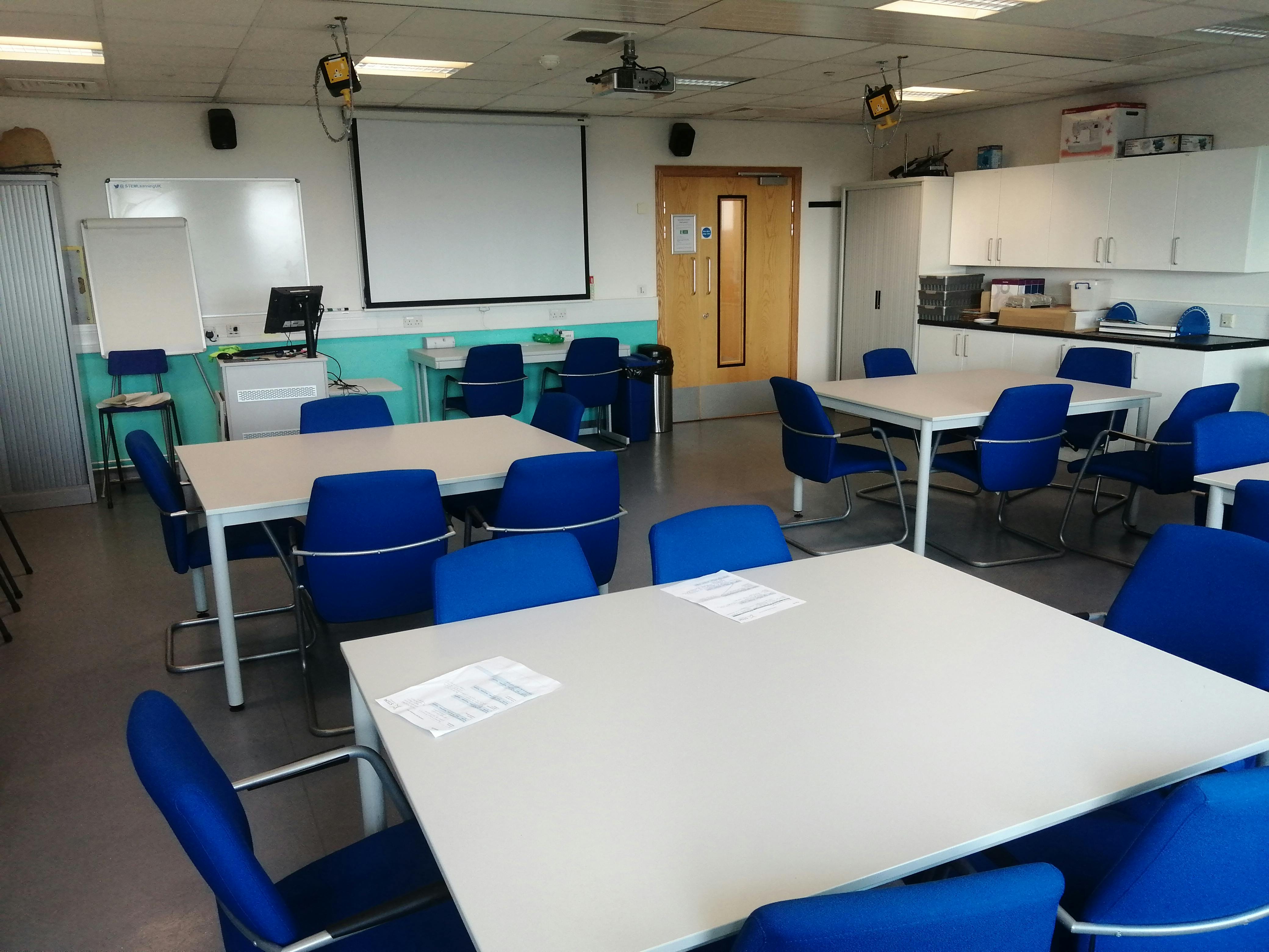 Versatile teaching room with blue chairs, ideal for STEM workshops and training sessions.