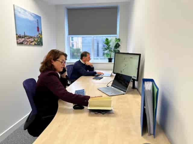 Focused professionals in a hybrid meeting with dual screens and plants for productivity.