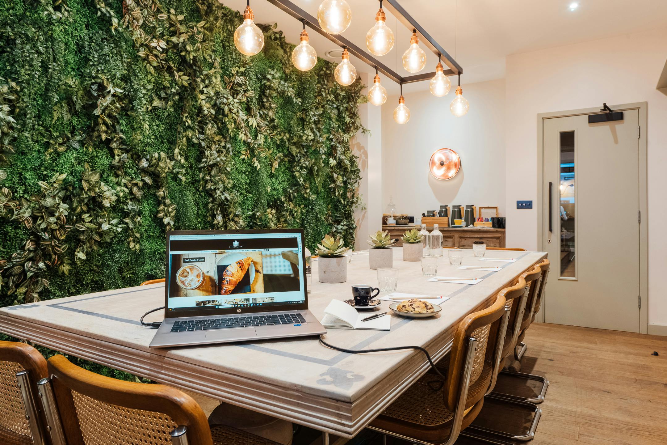 Modern meeting space with long table, lush green wall, ideal for collaboration events.