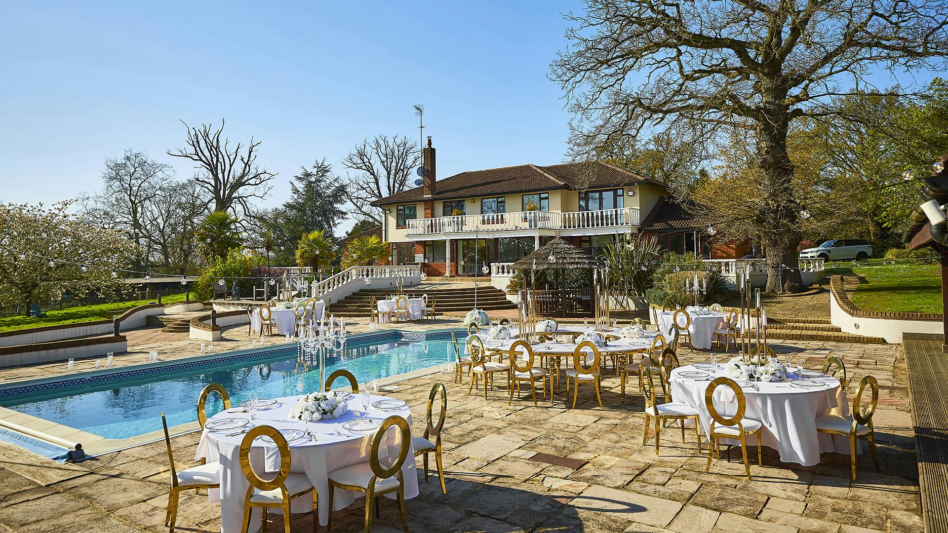 Elegant outdoor venue at The Villa Mansion with round tables by a sparkling pool.