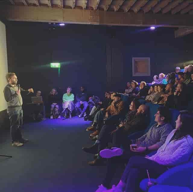 "Cozy Catford Mews cinema with speaker engaging audience for workshops and screenings."