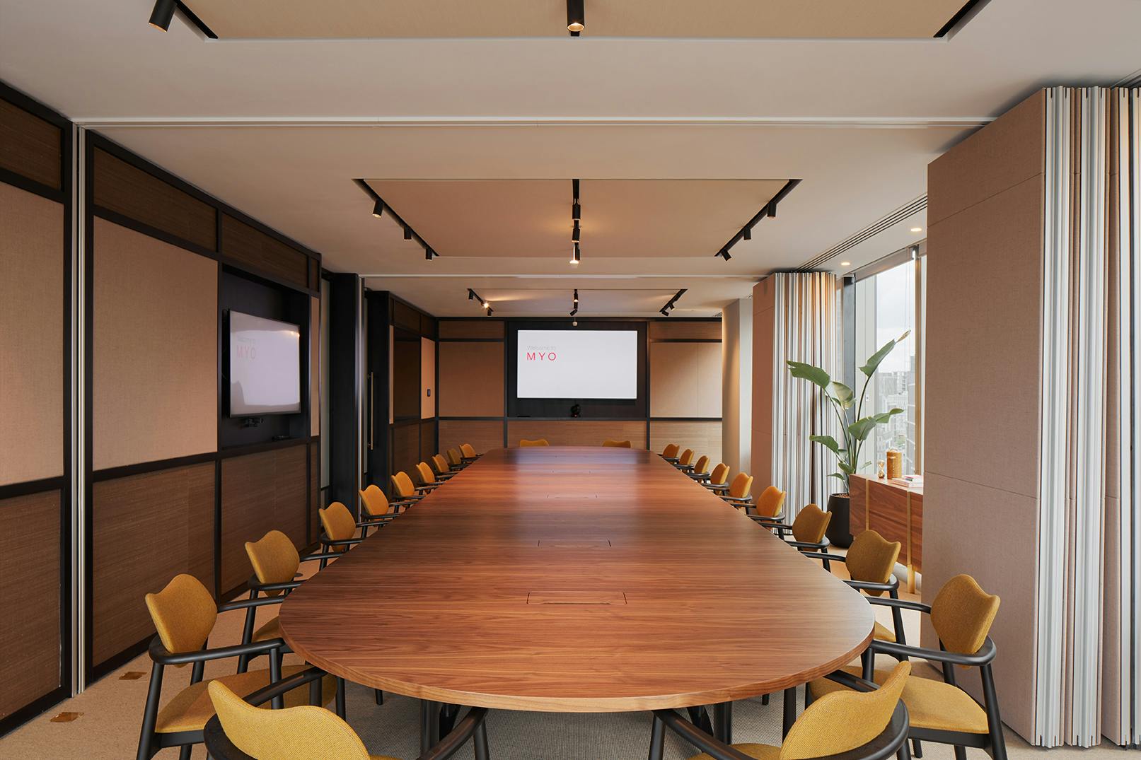 Modern conference room with oval table and dual screens for collaborative meetings.