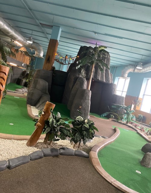 Vibrant indoor mini-golf venue with lush greenery for events in Birmingham. - Banner