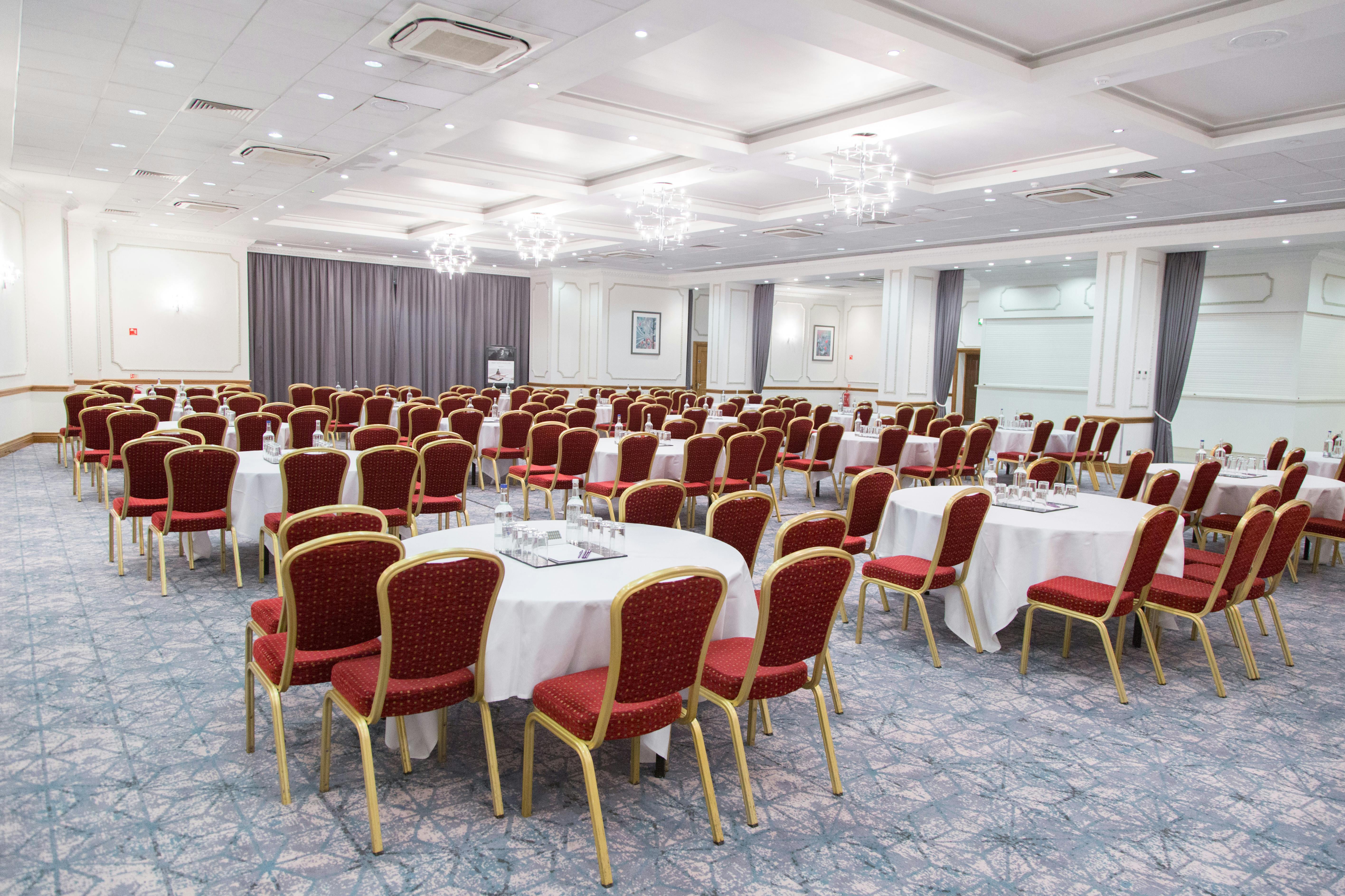 Wessex Suite conference space with round tables and red chairs, perfect for events.