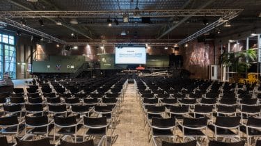 Spacious expo venue with black chairs and stage at Spoorweg Museum for conferences.