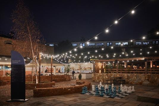 Outdoor event space with string lights and large chess set for social gatherings.