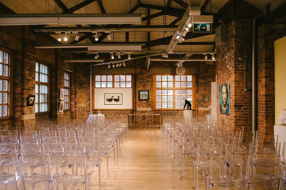 Versatile event space with acrylic chairs, exposed brick walls, ideal for meetings and gatherings.