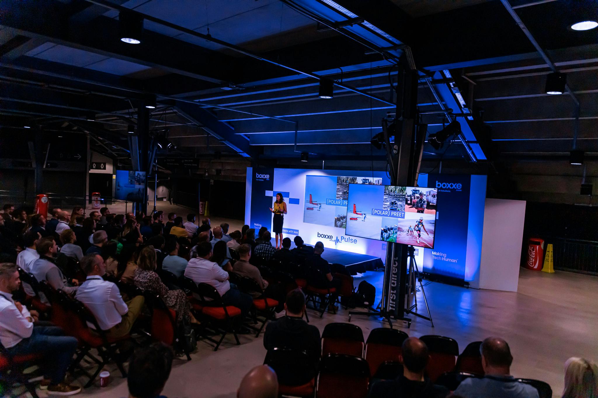 "First Direct Arena Leeds event space with speaker, screens, and engaged audience."