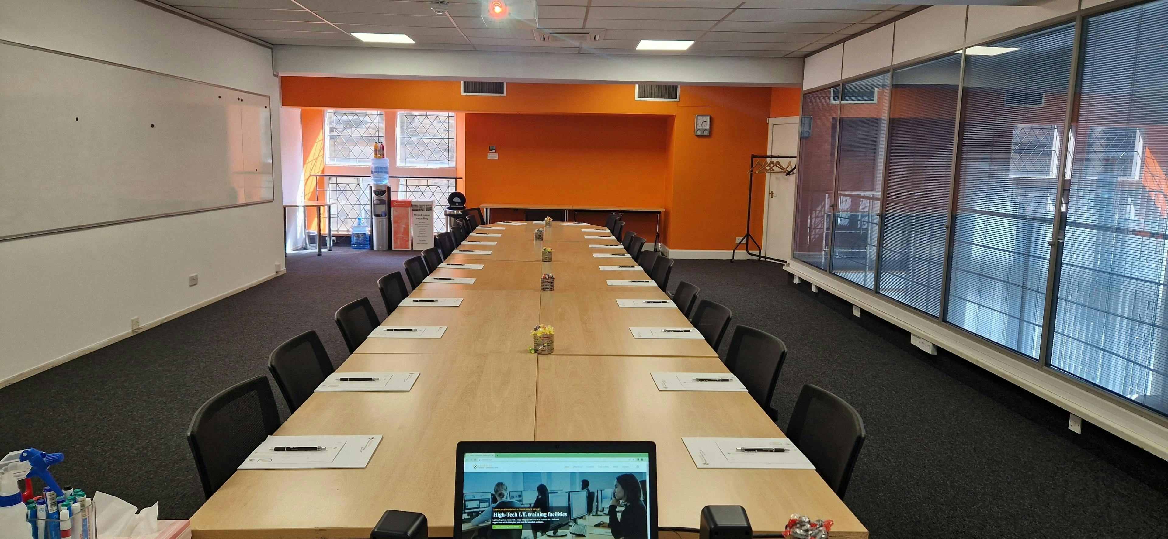 Meeting room with long table and orange wall, ideal for productive corporate events.