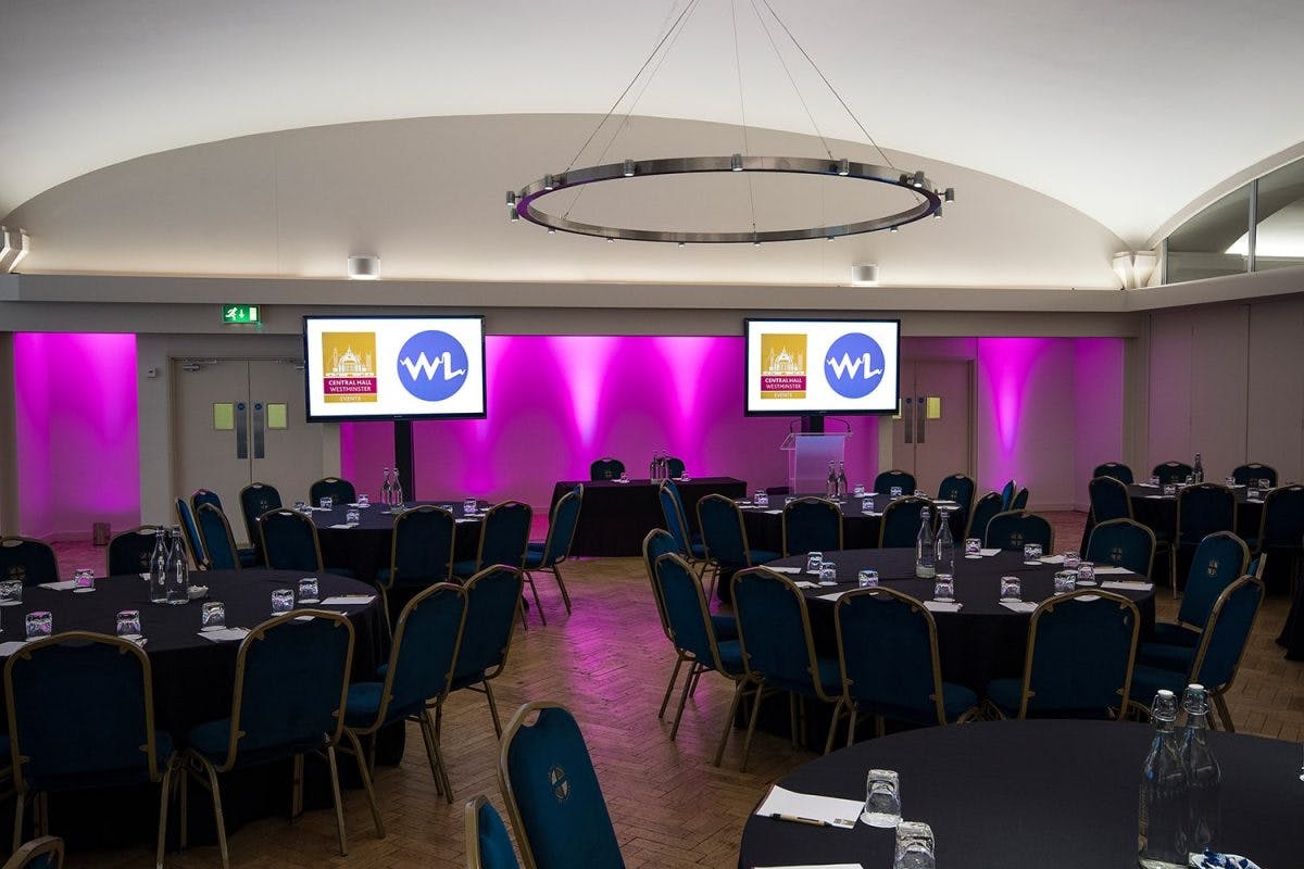 Elegant meeting room with round tables, purple uplighting for corporate events.