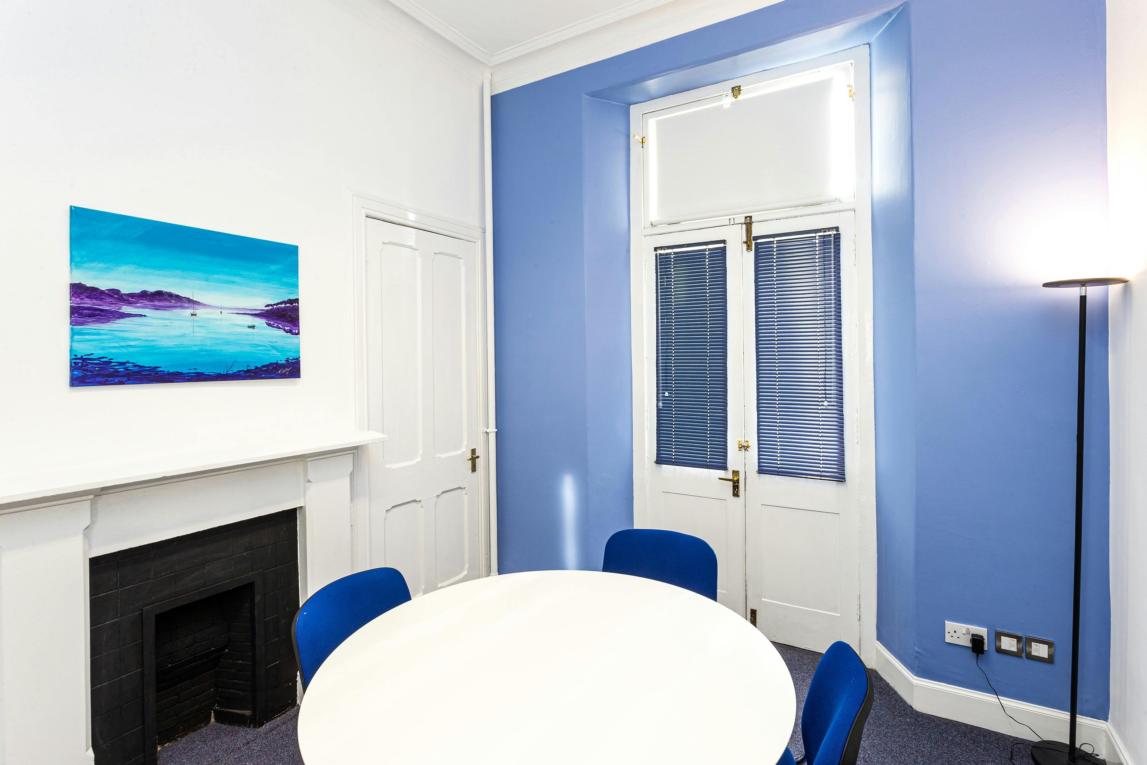 Bright boardroom with round table and blue chairs, ideal for meetings and collaborations.