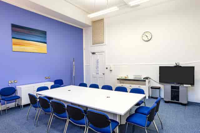 Interview room with large white table and blue chairs, perfect for workshops and meetings.