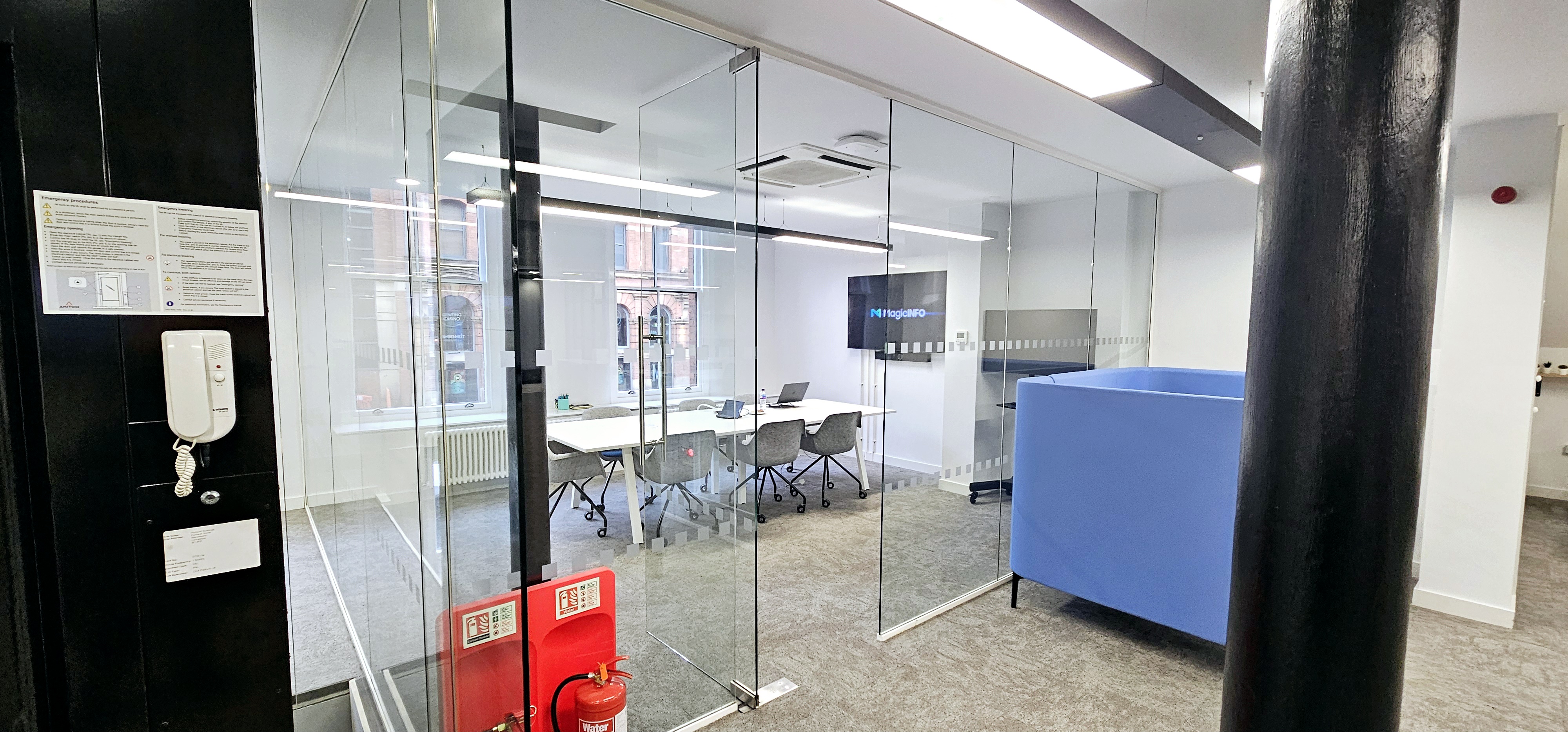 Modern meeting room with glass walls, blue seating for collaboration and brainstorming. - Banner