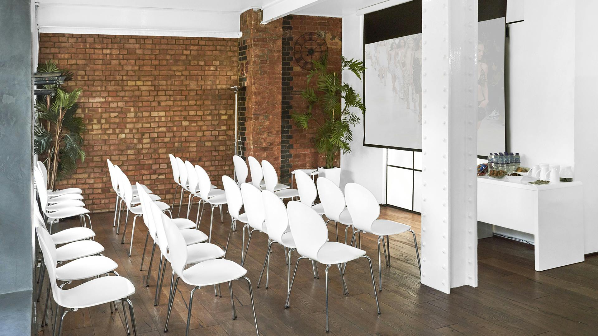 "Minimalist meeting space with white chairs and large screen for workshops or conferences."