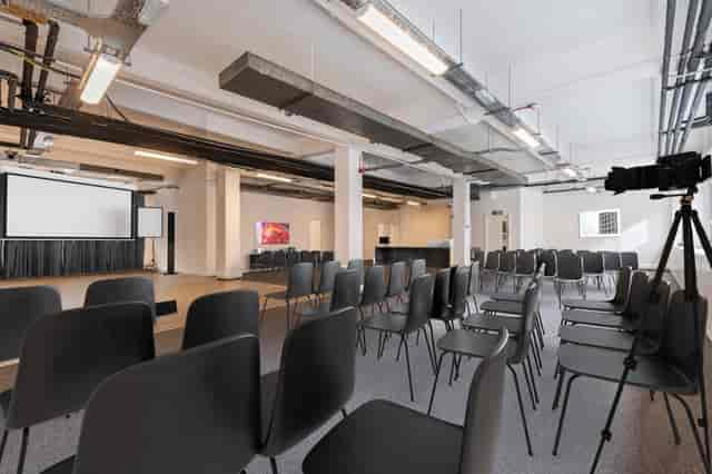 Versatile event space with black chairs and large screen, perfect for conferences or workshops.