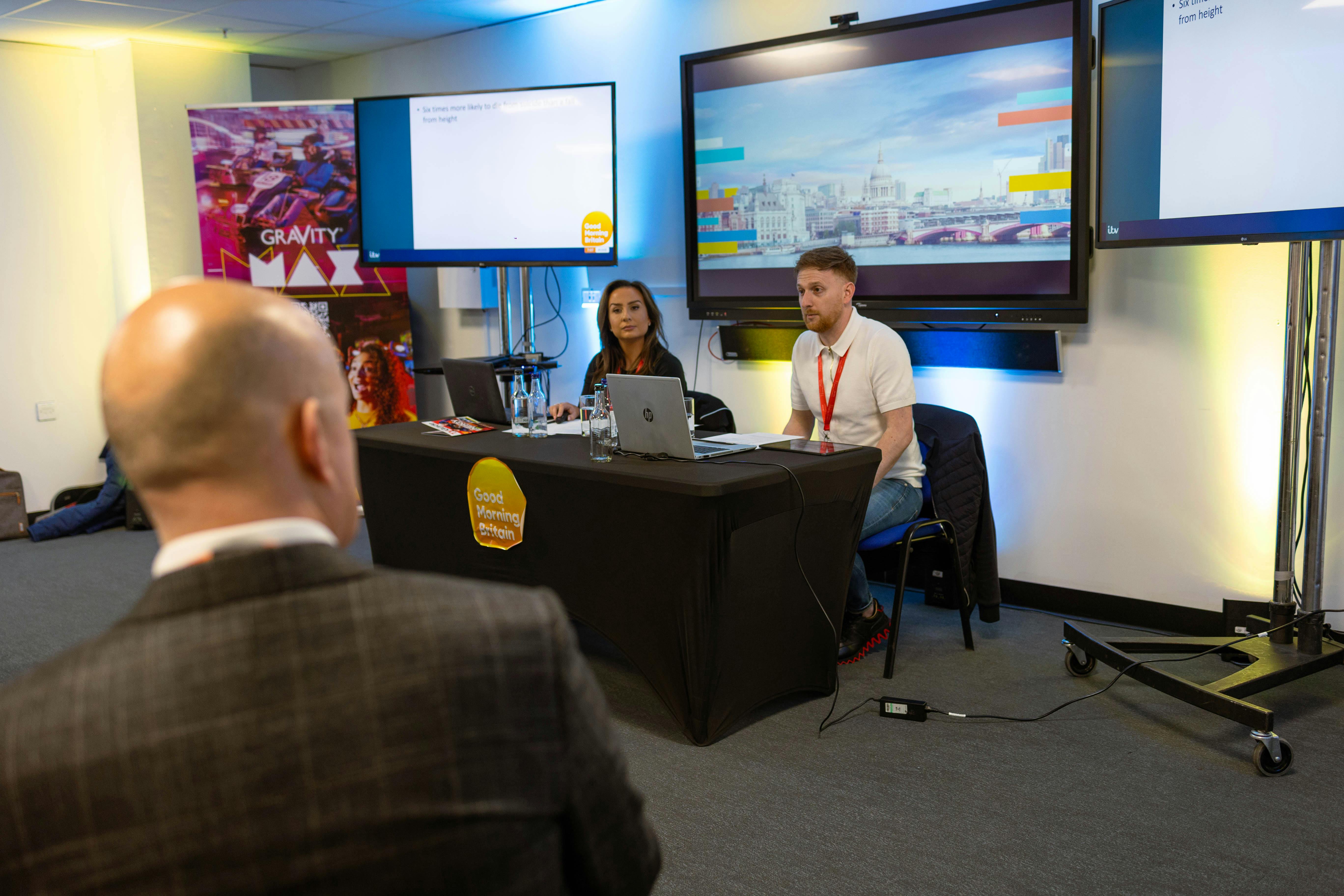 Professional panel discussion in Gravity Max meeting room with vibrant branding and digital screens.